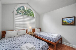 Ein Schlafzimmer mit zwei Betten, einem Fenster mit Jalousien, einer Nachttischlampe und einem Bild an der Wand.
