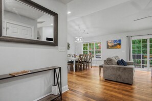 A spacious living area with a dining table, a gray sofa, and a large mirror.