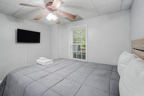 A bedroom with a bed, a ceiling fan, a TV, and a window with blinds.