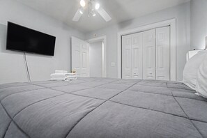 A bedroom with a bed, a flat-screen TV mounted on the wall, and a ceiling fan.