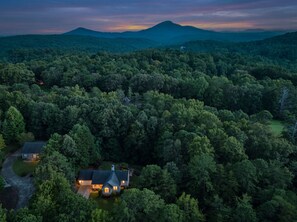 A house surrounded by dense forest with a mountain in the background.