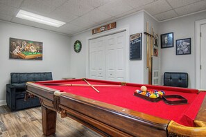 A pool room with a pool table, cue sticks, a dartboard, and a framed baseball player photo.