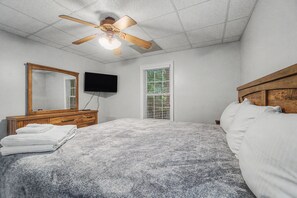A bedroom with a bed, a wooden dresser, a television, and a ceiling fan.