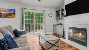 A living room with a sofa, a coffee table, a fireplace, and a large window with a view of greenery. - Sleeps 12 in  Innsbruck cabin near downtown Helen. (Helen)