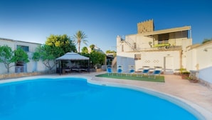 Una piscina con sedie a sdraio, una zona relax coperta e un edificio con un balcone.