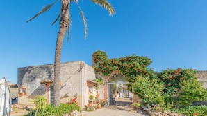 Un edificio tradizionale con una palma, un muro in pietra e un giardino fiorito.