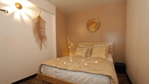 A bedroom with a wooden bed, a feather wall decoration, a heart-shaped wall art, and string lights. - THE DOLCE VITA SUITE (Sin-le-Noble)