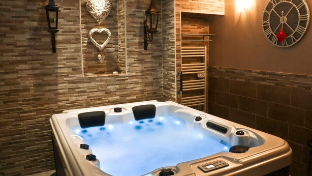 A modern bathroom with a hot tub, a clock, and decorative wall lights. - THE DOLCE VITA SUITE (Sin-le-Noble)