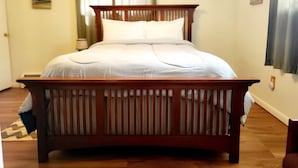 A bedroom with a wooden bed, white bedding, a nightstand, a lamp, and a painting on the wall. - Private and spacious apartment close to Cornell in quiet residential area. (Ithaca)