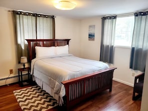 A bedroom with a wooden bed, a nightstand, a lamp, a rug, and curtains.