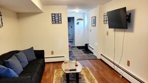 A living room with a black sofa, a coffee table, and a TV mounted on the wall. - Private and spacious apartment close to Cornell in quiet residential area. (Ithaca)