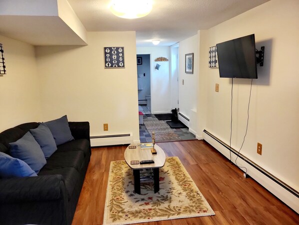 A living room with a black sofa, a coffee table, and a TV mounted on the wall.