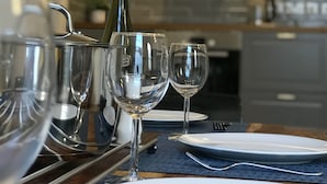 Ett matbord dukat med tallrikar, glas och en vinflaska, med ett modernt kök i bakgrunden.