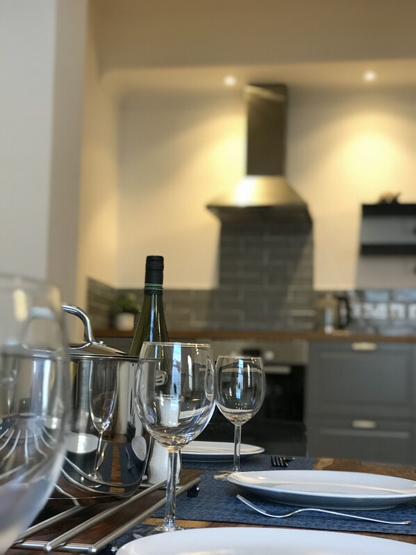 A dining table set with plates, glasses, and a wine bottle, with a modern kitchen in the background.