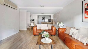 A modern living room with a leather sofa, a wooden coffee table, and a kitchen in the background. - 2 Spacious Resort 1BR Pool-Tennis-Gym & FREE Parkg (Perth)