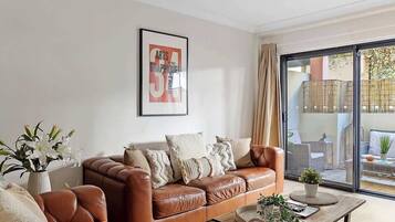 A modern living room with a brown leather sofa, a coffee table with a plant, and a large window with a view of the outside.