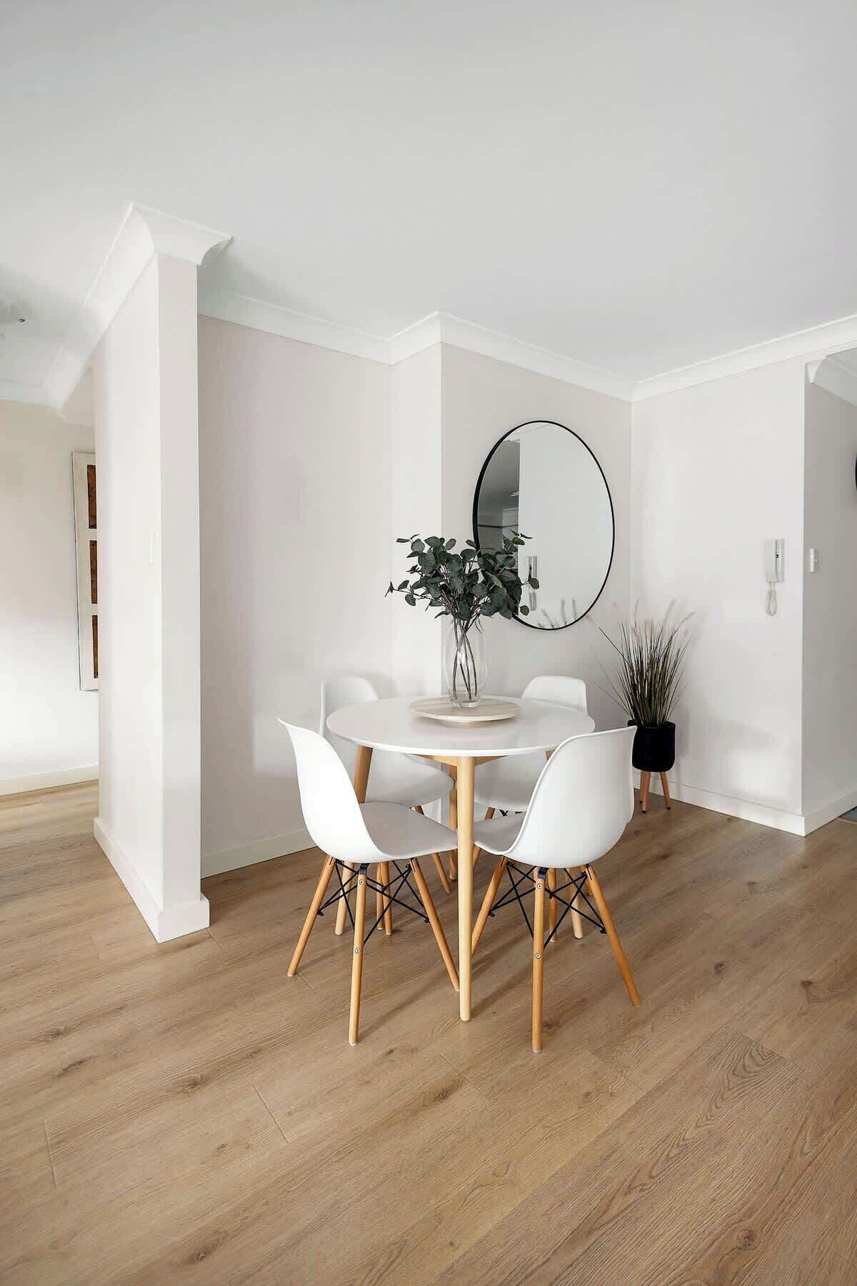 A modern dining area with a round table, white chairs, and a vase with greenery.
