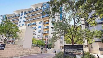 A multi-story residential building with balconies, a landscaped entrance, and a sign indicating 'MOUNT'S BAY VILLAGE' with directions to carparks and a restaurant.