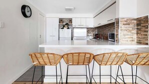 A modern kitchen with white cabinets, a large island, and a stone backsplash. There are wicker bar stools and a clock on the wall. - 2 Spacious Resort 1BR Pool-Tennis-Gym & FREE Parkg (Perth)