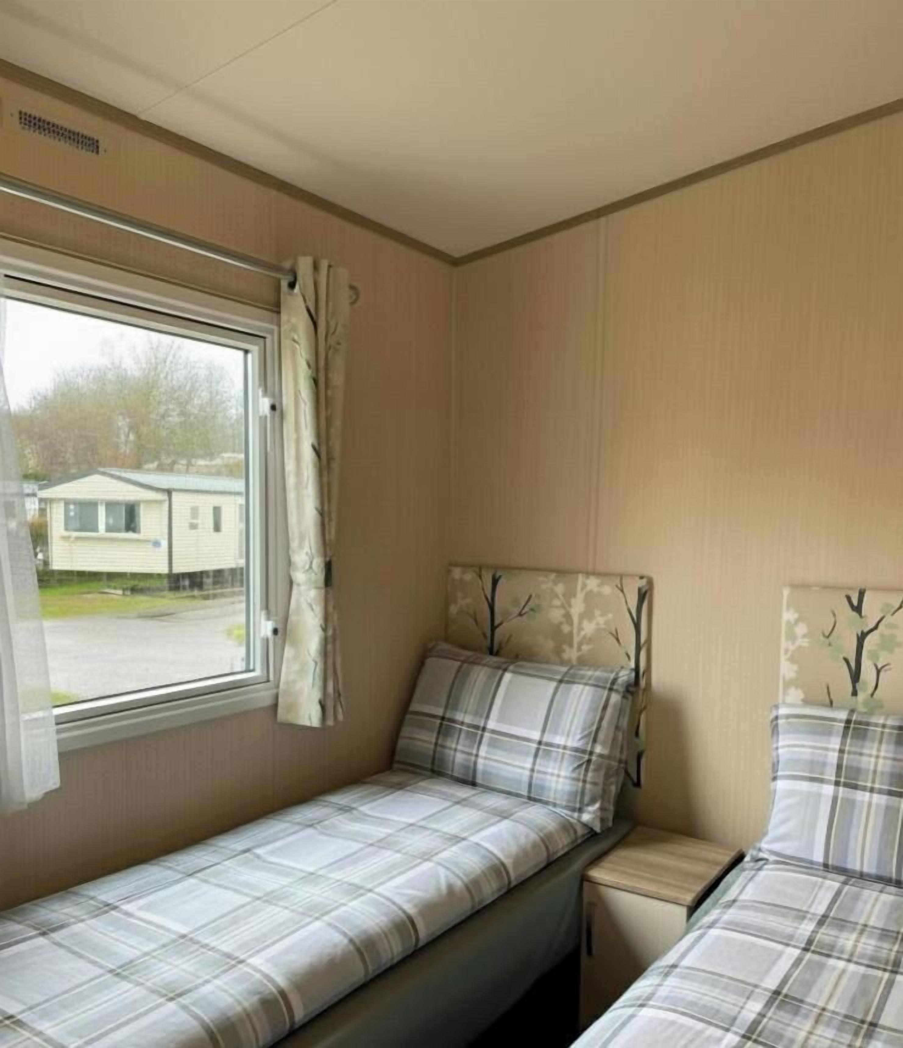 A room with two beds, a window with curtains, and a view of a house outside.