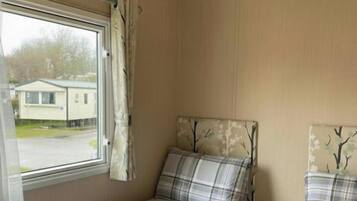 A room with two beds, a window with curtains, and a view of a house outside.