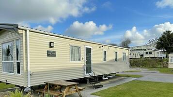 A mobile home with a nameplate, a picnic table, and potted plants.
