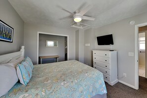 A bedroom with a bed, a dresser, a ceiling fan, a television, and a door leading to another room. - Some Beach | Oceanfront + Direct Beach Access! (Surf City)