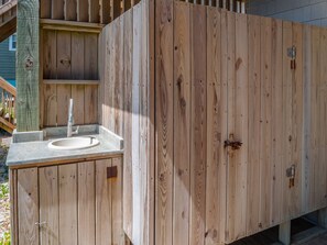 A wooden outdoor shower with a stone sink and a metal faucet.