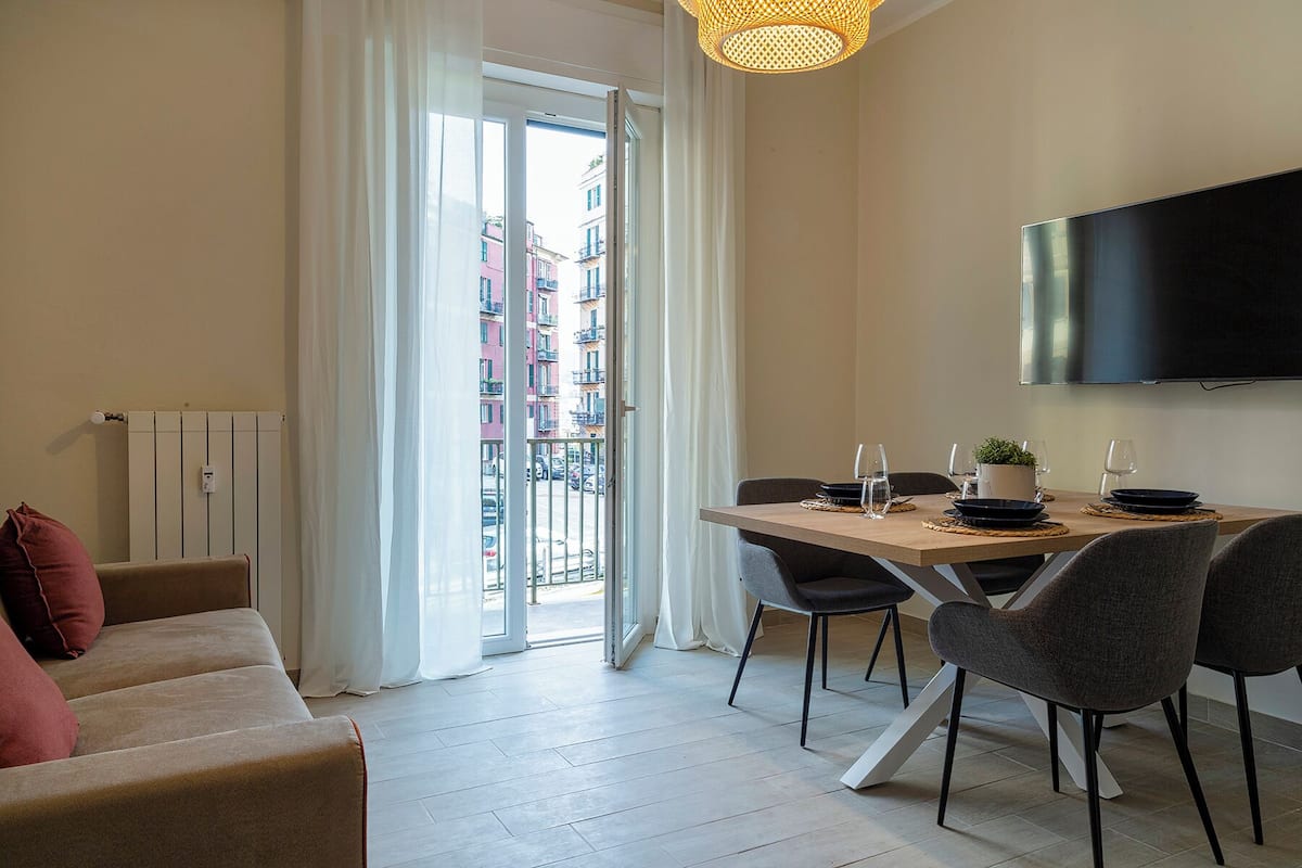 A modern living room with a sofa, a dining table set for two, and a TV mounted on the wall.