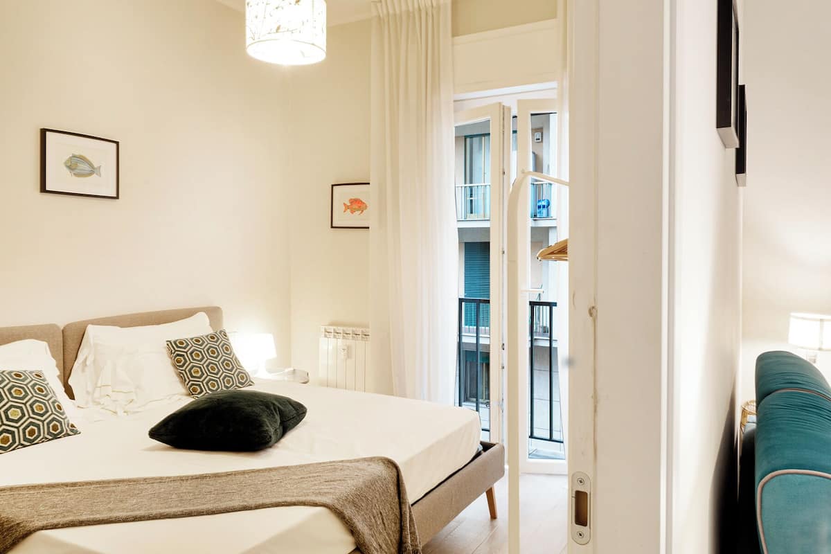 A bedroom with a bed, a bedside table, and a window with curtains.