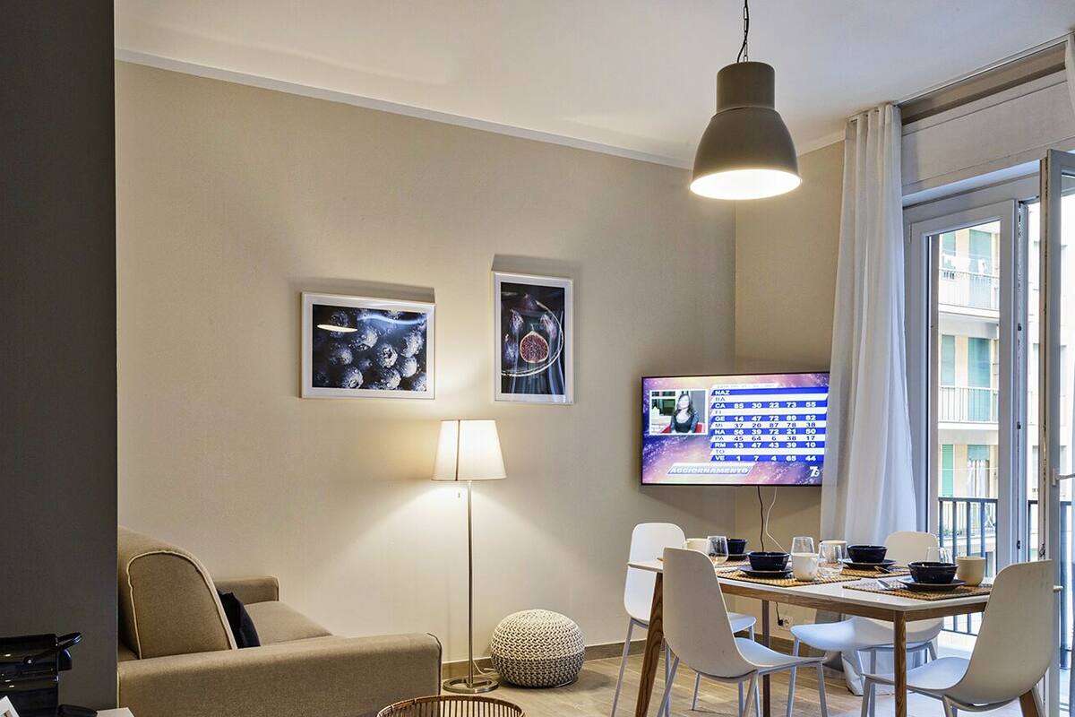 A modern living room with a sofa, a dining table with chairs, a floor lamp, and a TV mounted on the wall.