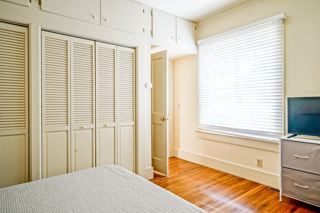 A bedroom with a bed, a TV, a wardrobe, and a window with blinds.