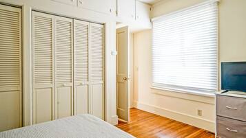A bedroom with a bed, a TV, a wardrobe, and a window with blinds.