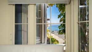 A room with a large window overlooking a street and a body of water. - Fountain Avenue - Pacific Grove Apartment - Steps to the Sea (Pacific Grove)