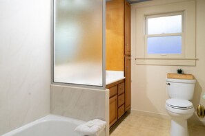 Un baño con bañera, armarios de madera, inodoro y ventana.