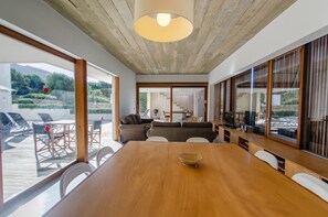 A spacious room with a wooden table, white chairs, a large window, and a view of the outdoor area. - Villa “Ses Alzines” with Sea View, Pool, A/C, Wi-Fi, Balcony, Garden & Terrace (Sant Lluís)