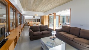 A modern living area with a wooden ceiling, two brown sofas, a white coffee table, and a kitchen in the background. - Villa “Ses Alzines” with Sea View, Pool, A/C, Wi-Fi, Balcony, Garden & Terrace (Sant Lluís)