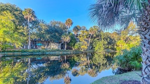 A serene park with a pond reflecting trees and a building with outdoor seating. - Coastal family friendly home, Lagoon View, walkable to beach - 25 Fairway Oaks (Isle of Palms)