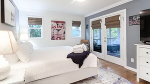 A bedroom with a bed, a nightstand, a lamp, a TV, and a door leading to a balcony. - Coastal family friendly home, Lagoon View, walkable to beach - 25 Fairway Oaks (Isle of Palms)