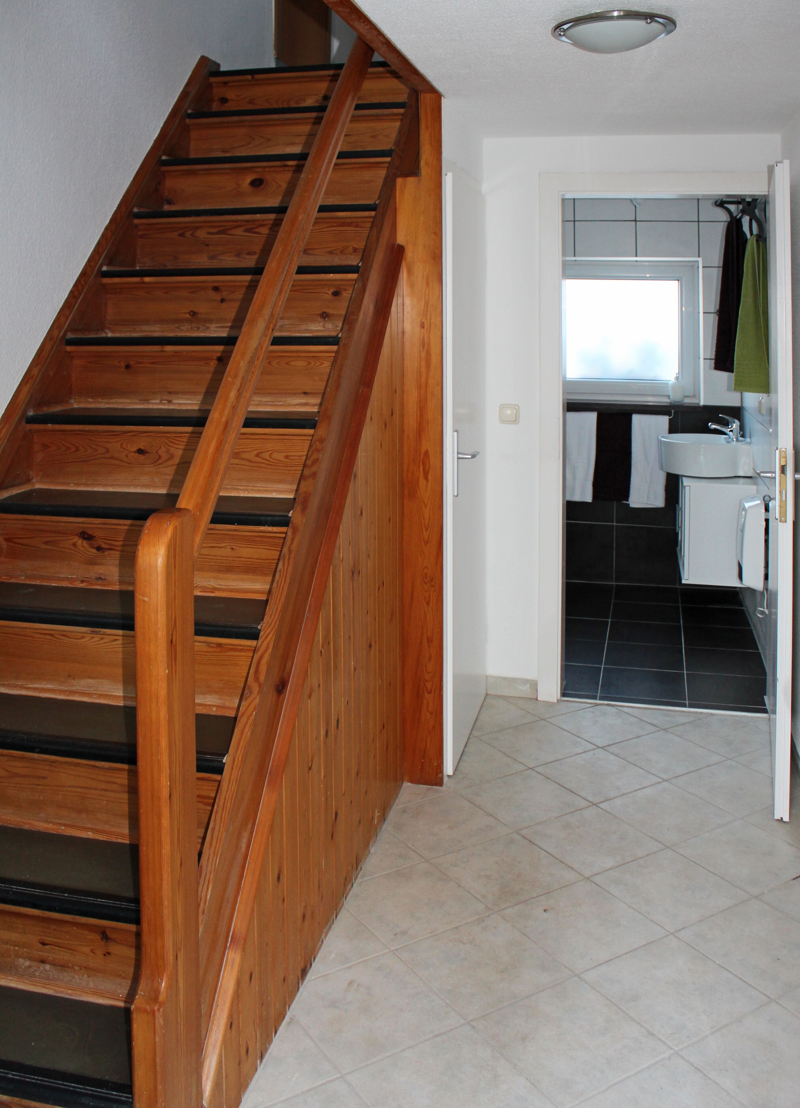 Eine Holztreppe führt zu einem Badezimmer mit Fenster und Waschbecken.
