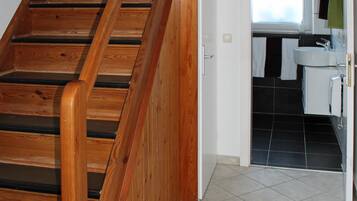 Eine Holztreppe führt zu einem Badezimmer mit Fenster und Waschbecken.