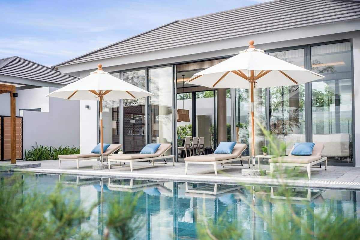 Een modern buitenzwembad met ligbedden en parasols, grote ramen en een helder uitzicht op het omliggende groen.
