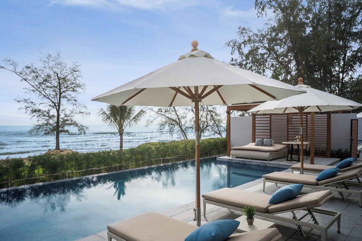 Un espace aménagé au bord de la piscine, avec des chaises longues et des parasols, offrant une vue sur l’océan.