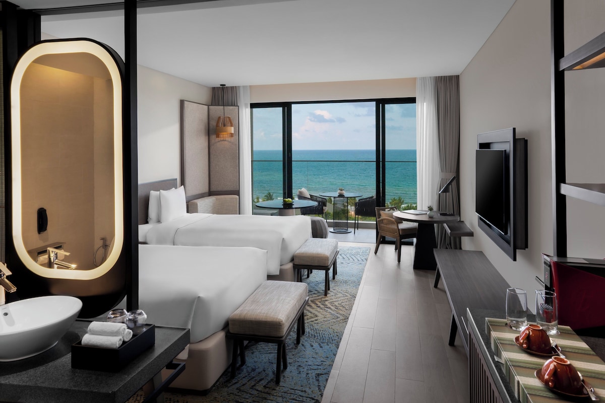 Une chambre d’hôtel avec un grand lit, un bureau, une télévision et une vue sur l’océan.