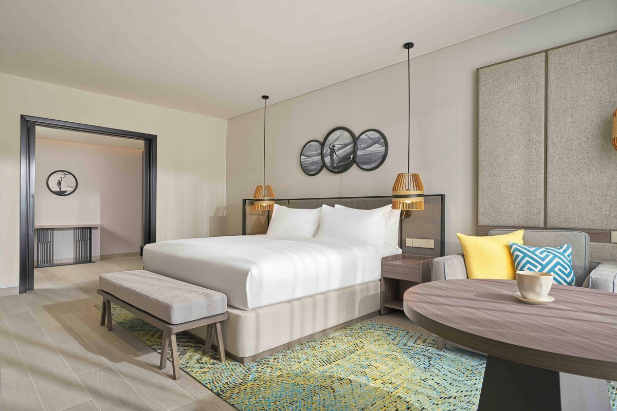 Een moderne hotelkamer met een groot bed, nachtkastjes, een ronde salontafel en een zithoek.