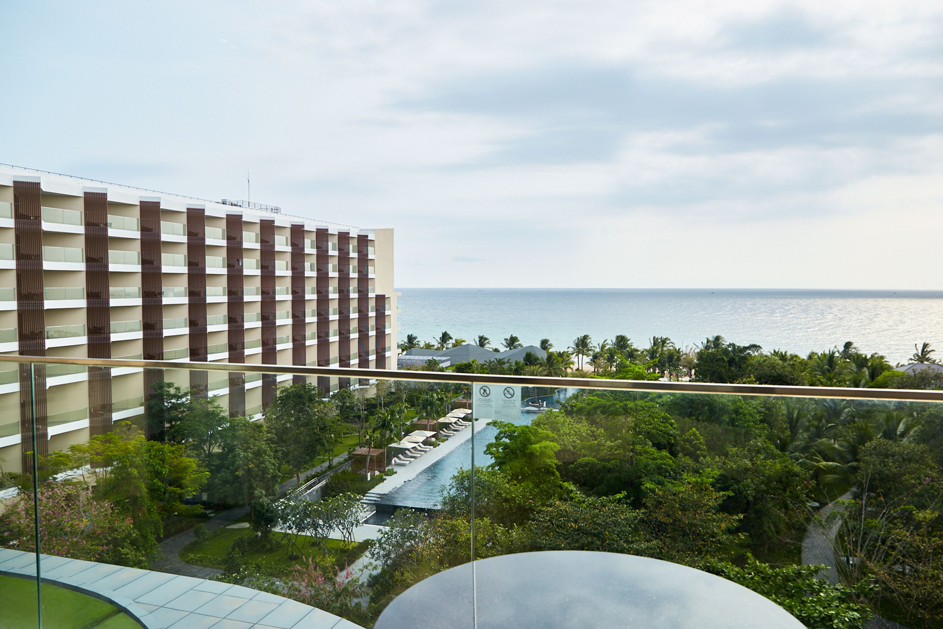 A high-rise hotel with a view of the ocean, lush greenery, and a swimming pool.