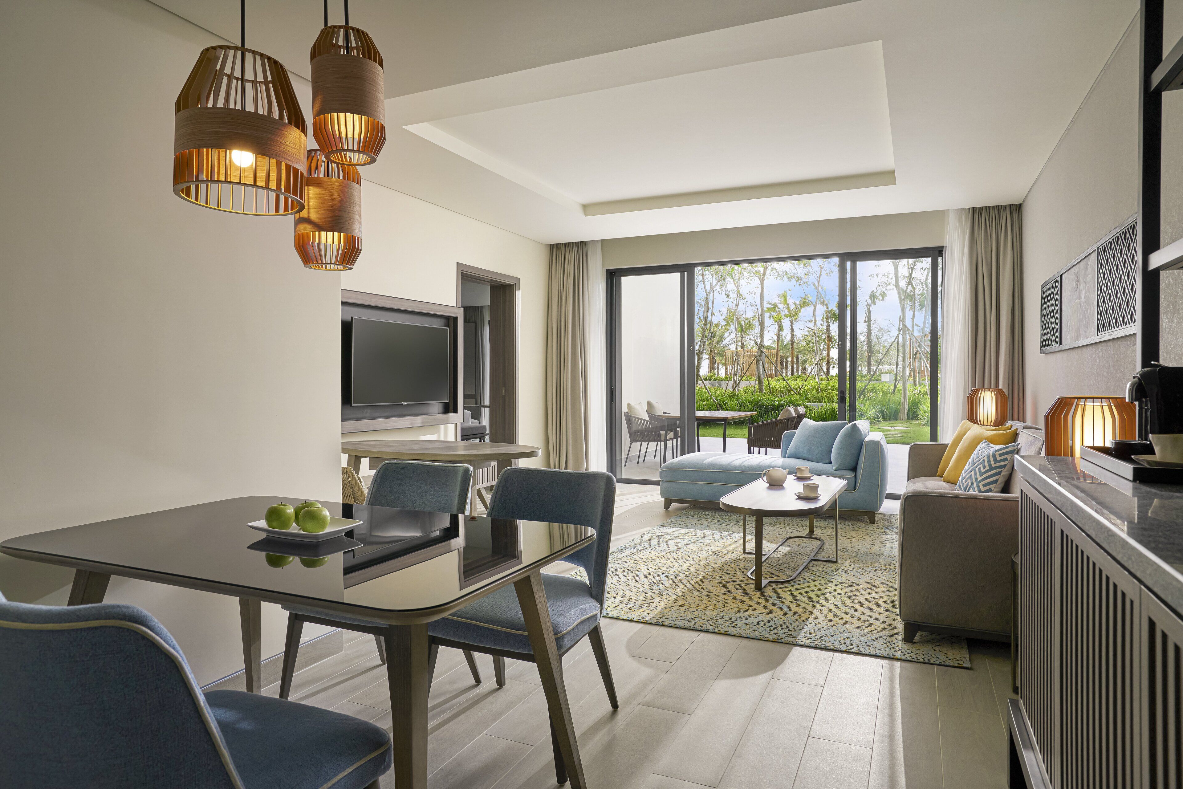 A modern living room with a dining area, large windows, and a view of greenery.