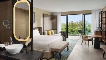 Una habitación de hotel moderna con una cama grande, un espejo redondo, un lavamanos, un banco, una mesa de comedor y un balcón con vistas a zonas verdes.