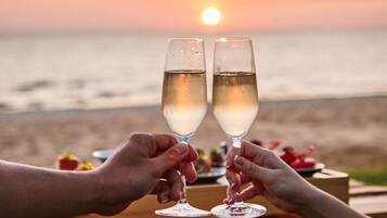 Dos personas brindando con copas de champán sobre una mesa de madera, con un atardecer de fondo.