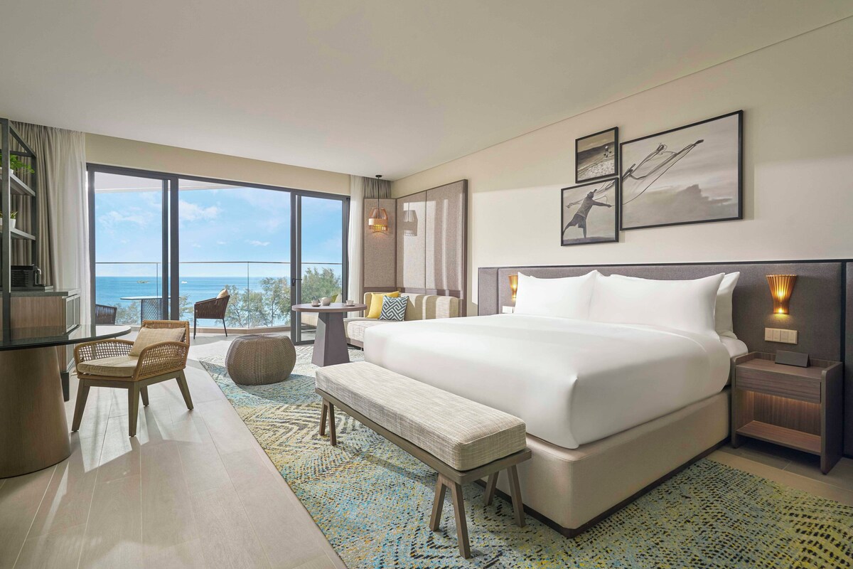 Een hotelkamer met een groot bed, een zithoek met een tafel en uitzicht op zee.